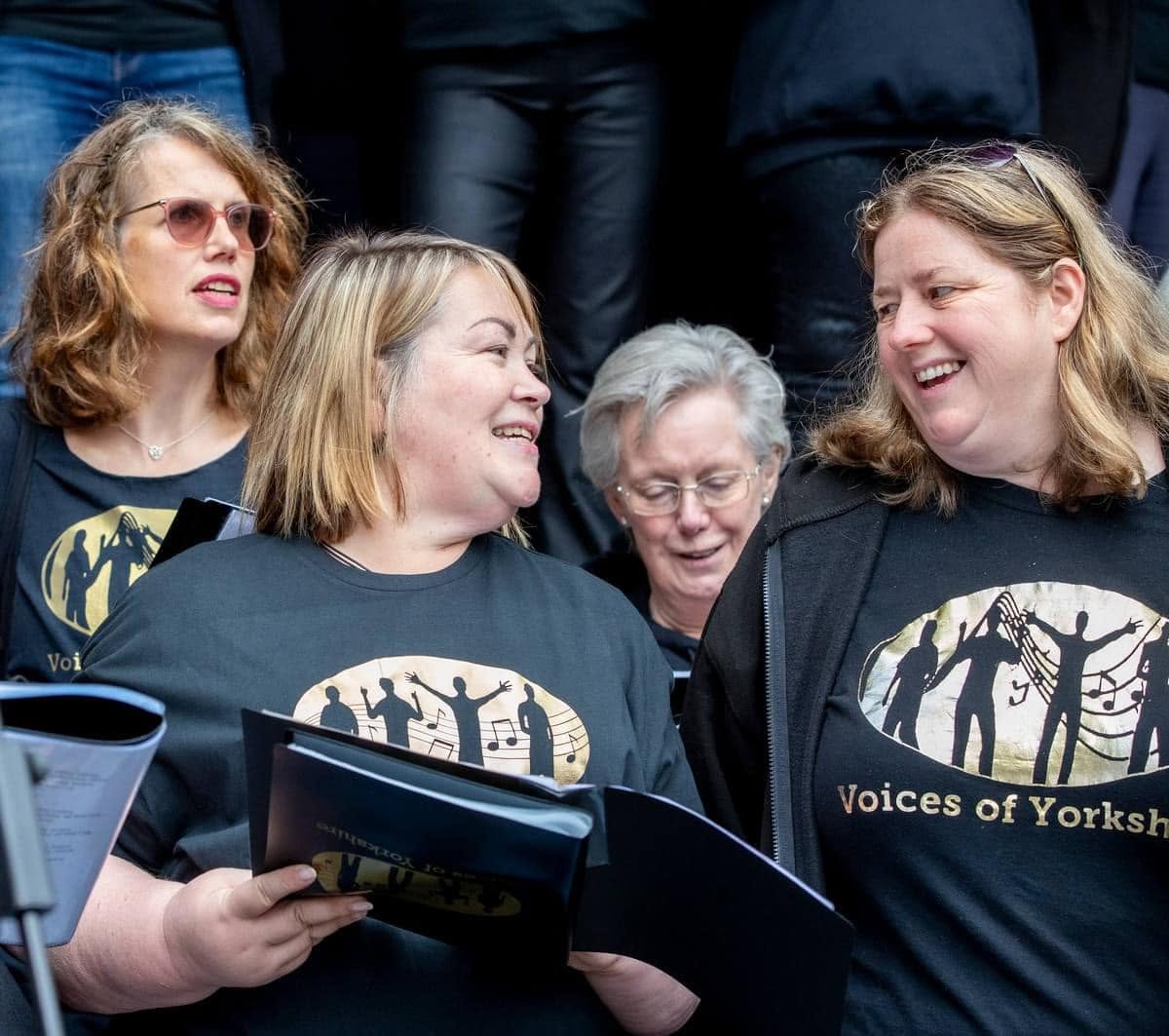 Three VOY members laughing together in their gold logo t-shirts